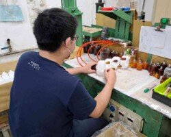 作業員在工作台前對多個白色零件進行氣密測試,零件連接至紅色測試軟管,周圍設有壓力表與檢測設備。