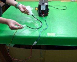 作業員在綠色工作檯上進行點燈測試,將半透明零件接通電源,並透過測試機台上的電流表監測狀態。